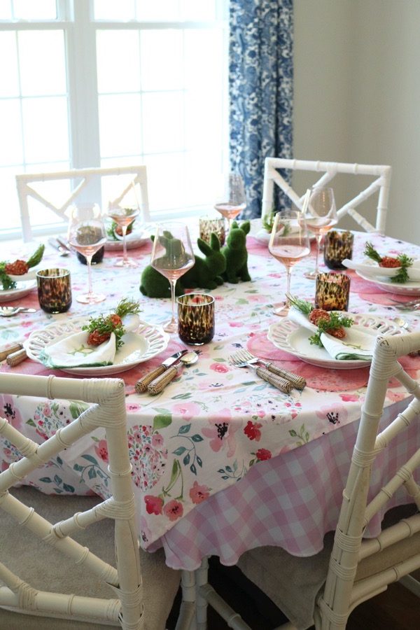 A floral Easter themed table with colorful glassware, linen napkins and bunnies at the center.