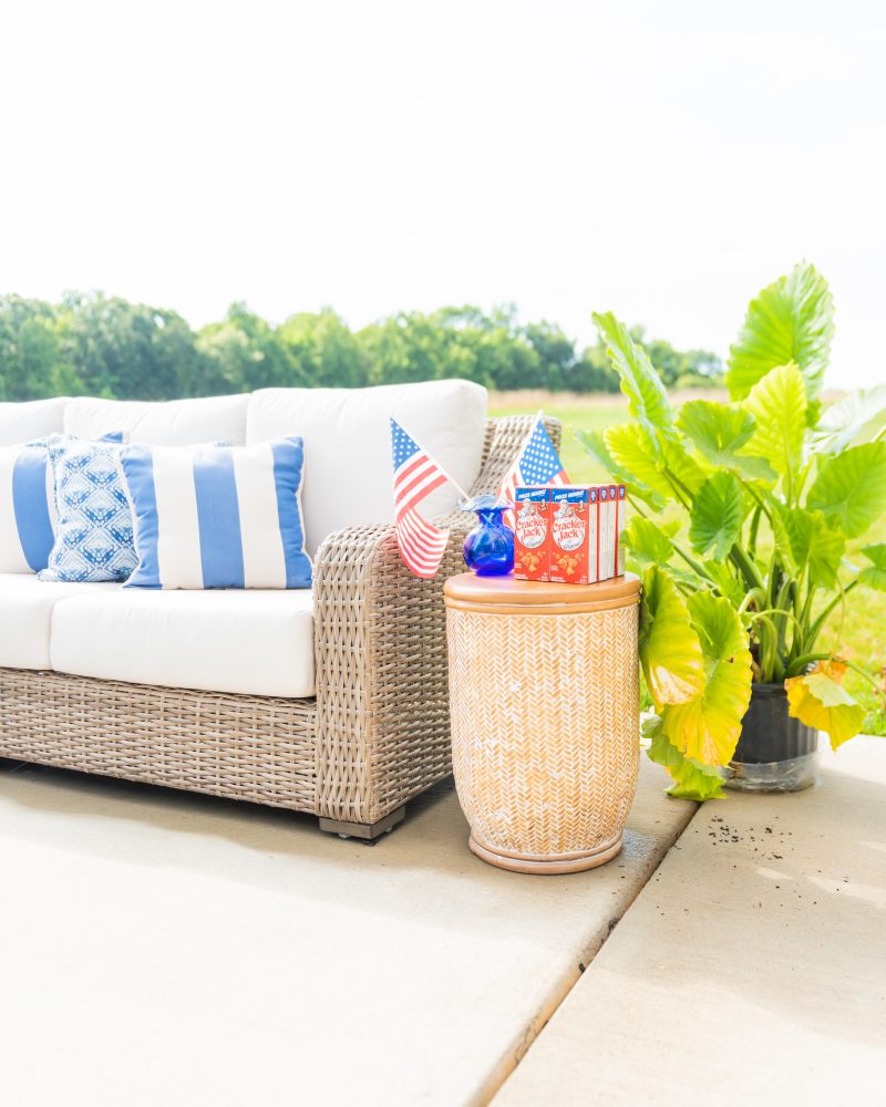 Rows of cracker jack snacks are lined up next to two American flags for decoration on the patio.